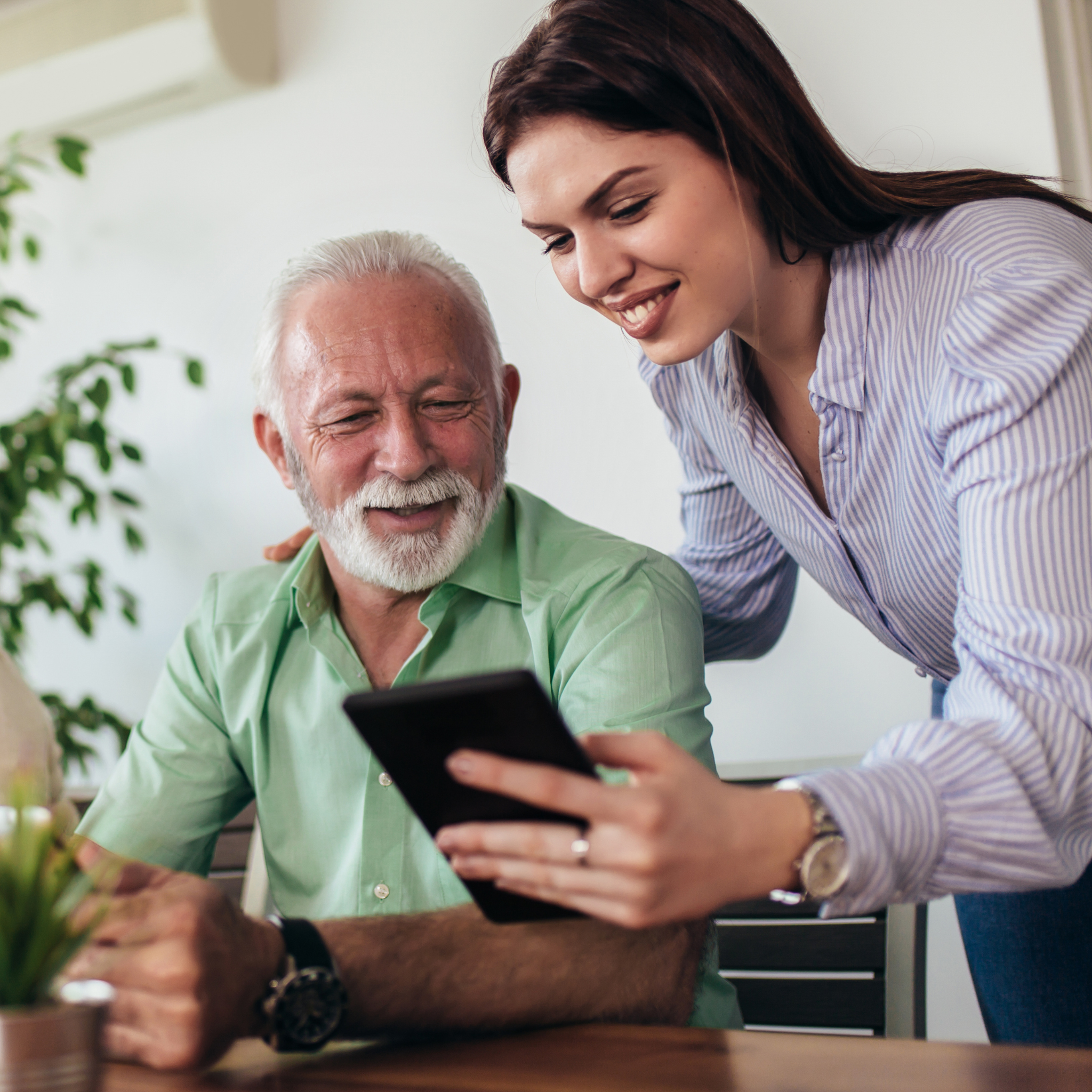 A young woman showing an elderly man information on a tablet.