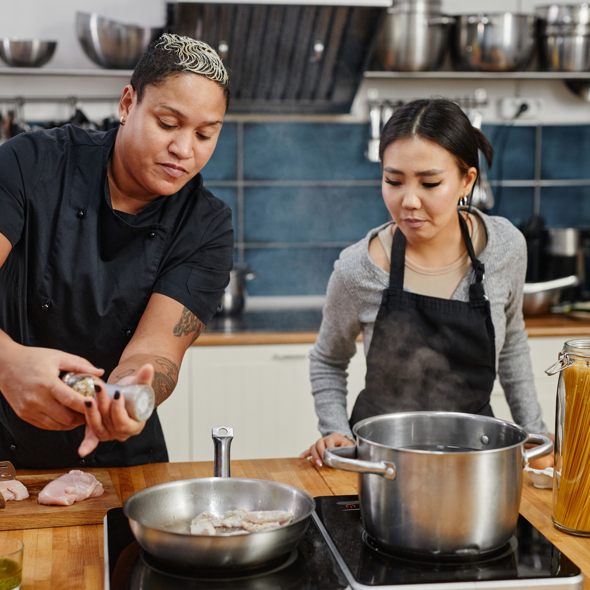 Two women standing over a stove in a kitchen